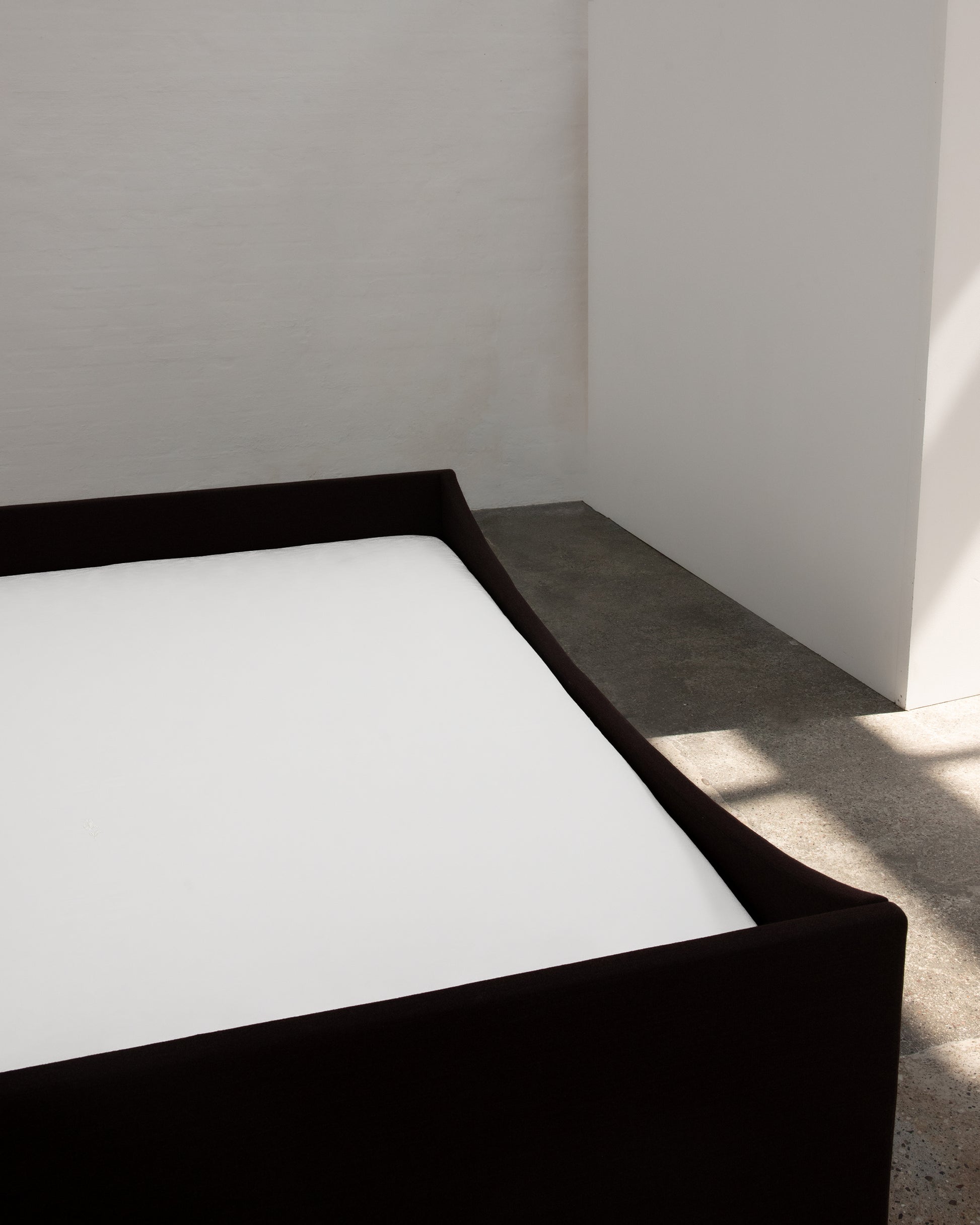 Minimalist black bed frame with white mattress against a plain wall.